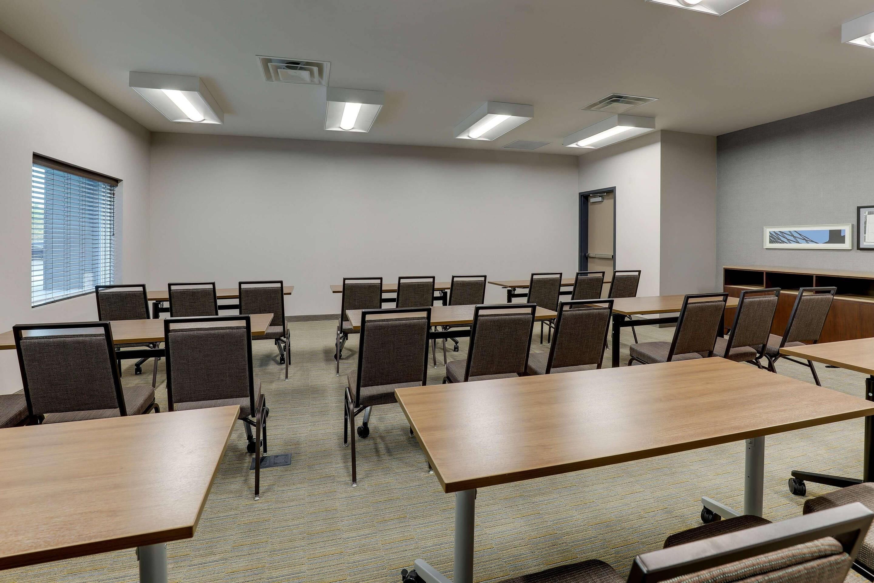 A conference room with multiple tables and chairs, ceiling lights, and a window with blinds.