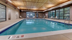 An indoor swimming pool with a wooden ceiling, clear glass windows, and a tiled edge.