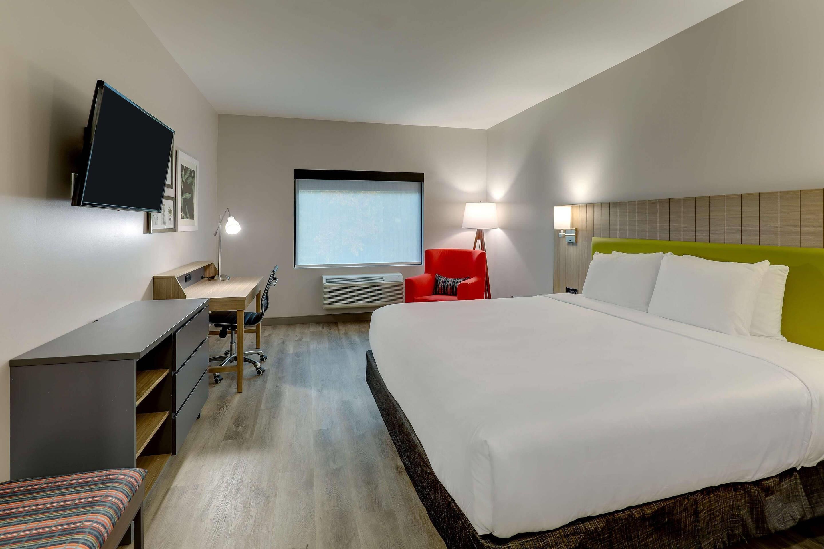 A hotel room with a bed, desk, chair, TV, and window.