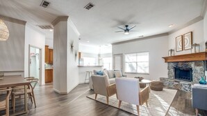 A spacious living room with a fireplace, a dining area with a wooden table and chairs, and a kitchen in the background. - Relax by fire pit - Walk to Lake (Little Elm)