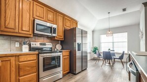 A modern kitchen with wooden cabinets, stainless steel appliances, and a dining area with a table and chairs. - Relax by fire pit - Walk to Lake (Little Elm)