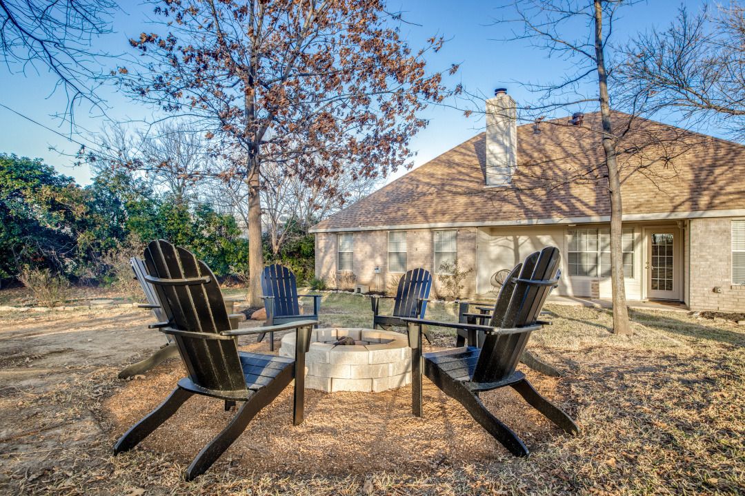 A house with a fire pit and Adirondack chairs in the backyard.
