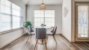 A dining area with a round table, four grey chairs, a hanging light fixture, and a window with blinds. - Relax by fire pit - Walk to Lake (Little Elm)