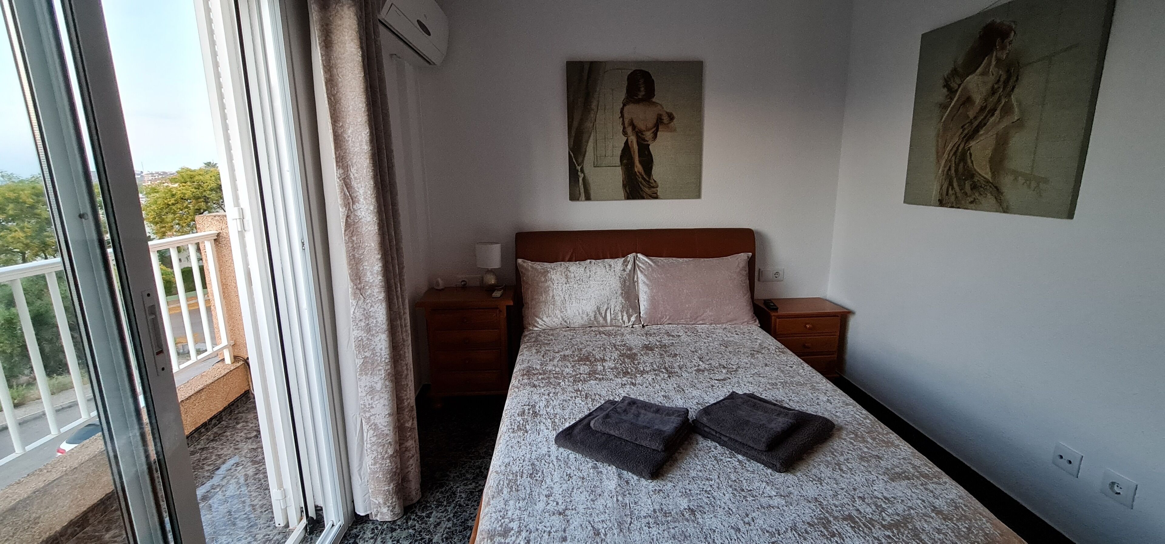 A hotel room with a bed, a nightstand, a painting on the wall, and a view of the outside balcony.