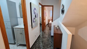 A hallway with a kitchen area on the left, a wooden cabinet, and a small table with a potted plant. - Surise Den- Walk to the beach, sea view and pool. Holiday rentals & winter stays (Puerto de Mazarrón)