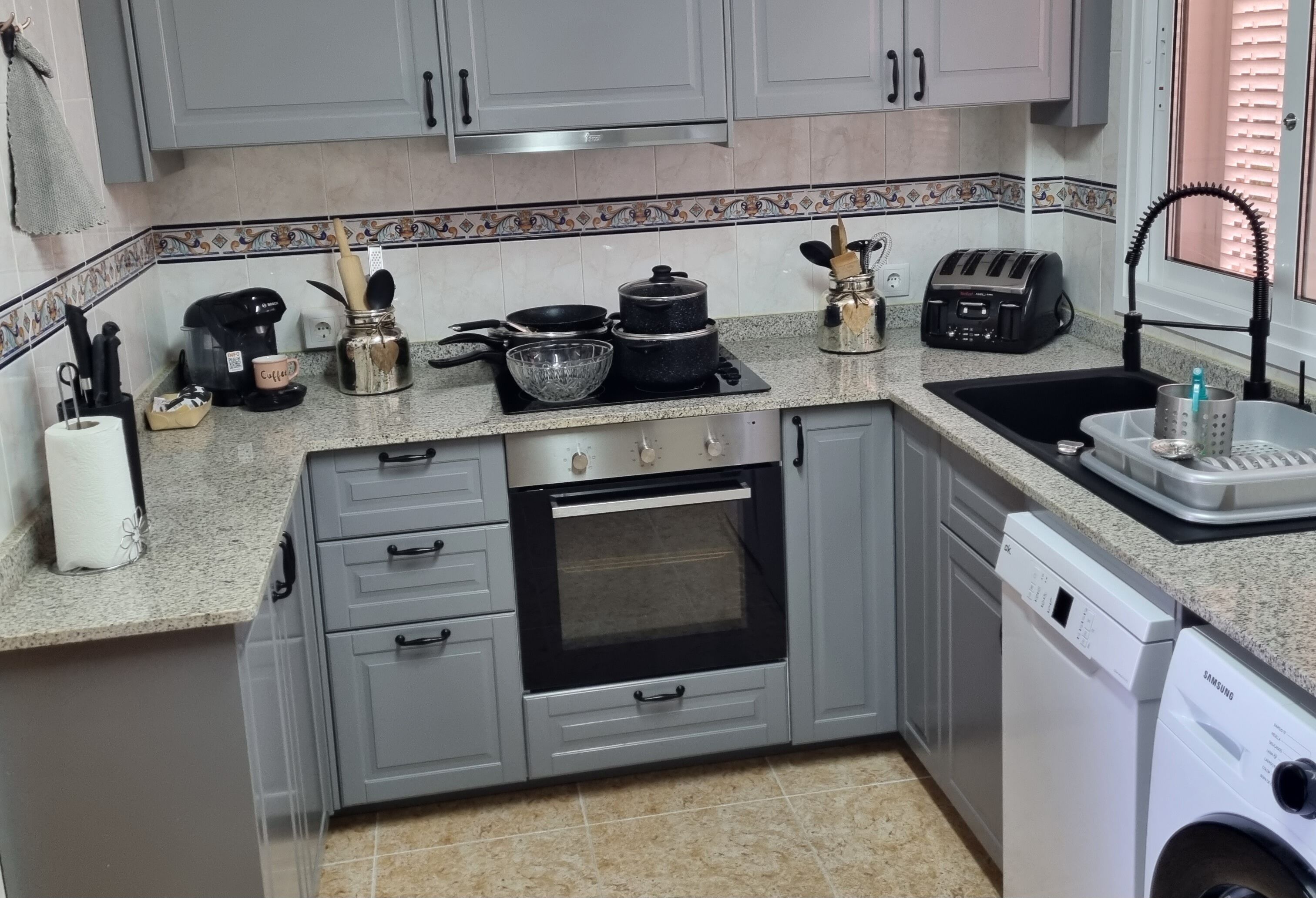 A kitchen with grey cabinets, a stainless steel oven, a coffee maker, a toaster, and a washing machine.