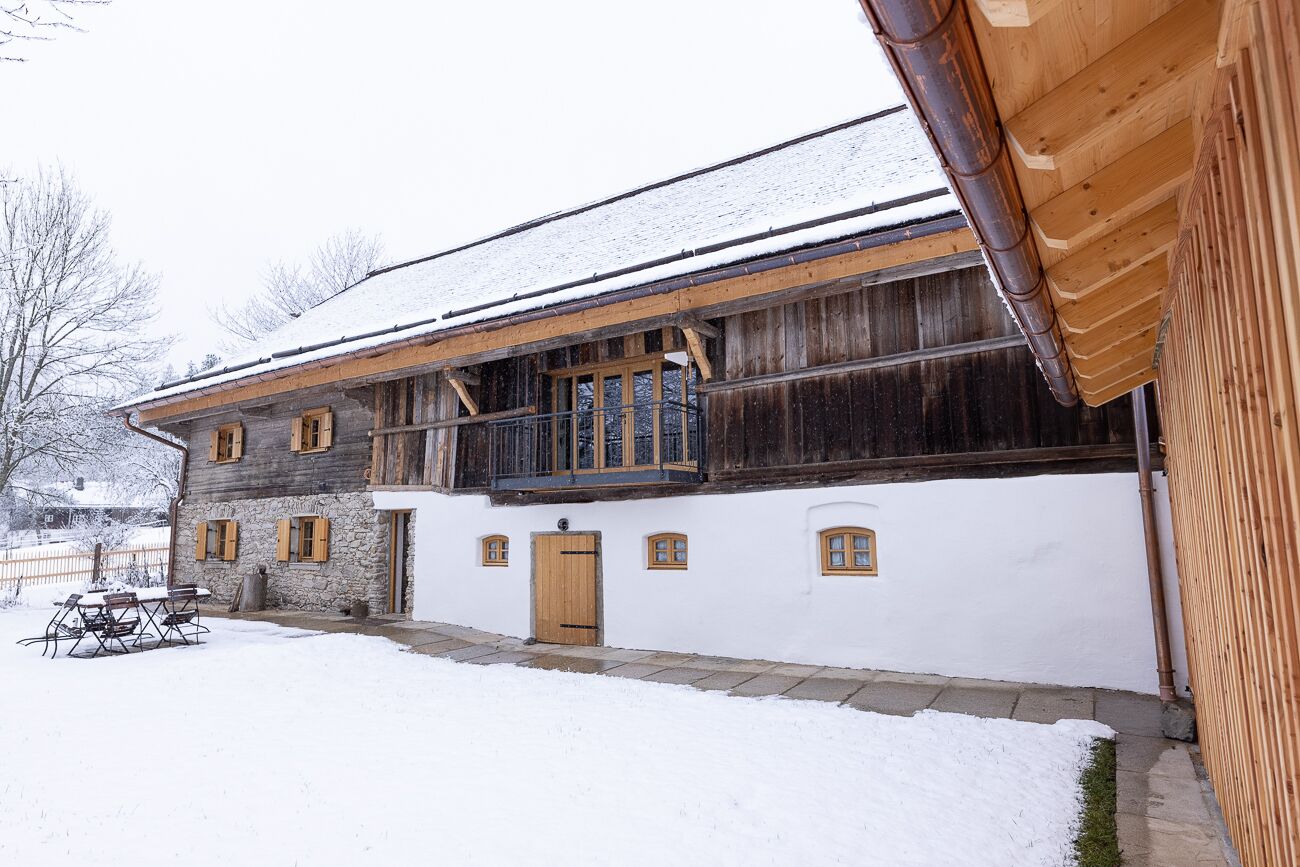 A traditional wooden building with a stone foundation, a balcony, and a snow-covered ground.
