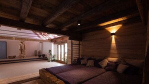 Interior de una cabaña de madera con una cama grande, tragaluz y una escultura de piedra.
