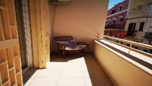 Ein schmaler Balkon mit einem Stuhl und einem kleinen Tisch, einem Fliesenboden und Blick auf Gebäude im Hintergrund.