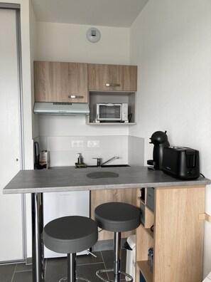 Une cuisine compacte équipée d’un four à micro-ondes, d’une machine à café et de deux tabourets.