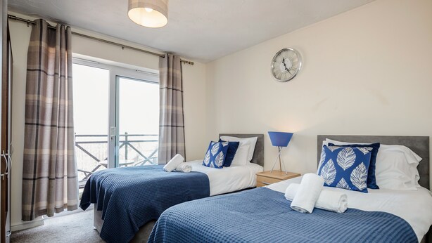 A hotel room with two beds, a clock on the wall, and a balcony view. - Captivating 3-bed Apartment in Grays (Grays)