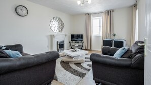 A modern living room with two dark sofas, a white coffee table, a fireplace, a flat-screen TV, and a decorative wall piece. - Captivating 3-bed Apartment in Grays (Grays)