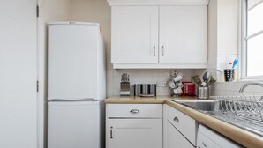 A compact kitchen with white cabinets, a built-in dishwasher, and a window above the sink. - Captivating 3-bed Apartment in Grays (Grays)