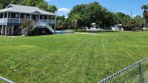 A large house with a covered porch, a swimming pool, and a boat docked in the background.