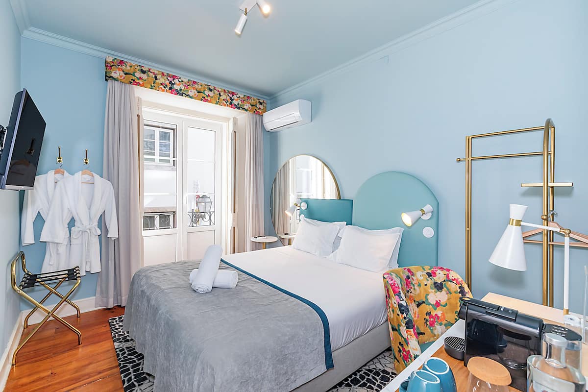 A hotel room with a bed, a desk with a coffee machine, a TV, and a window with curtains.
