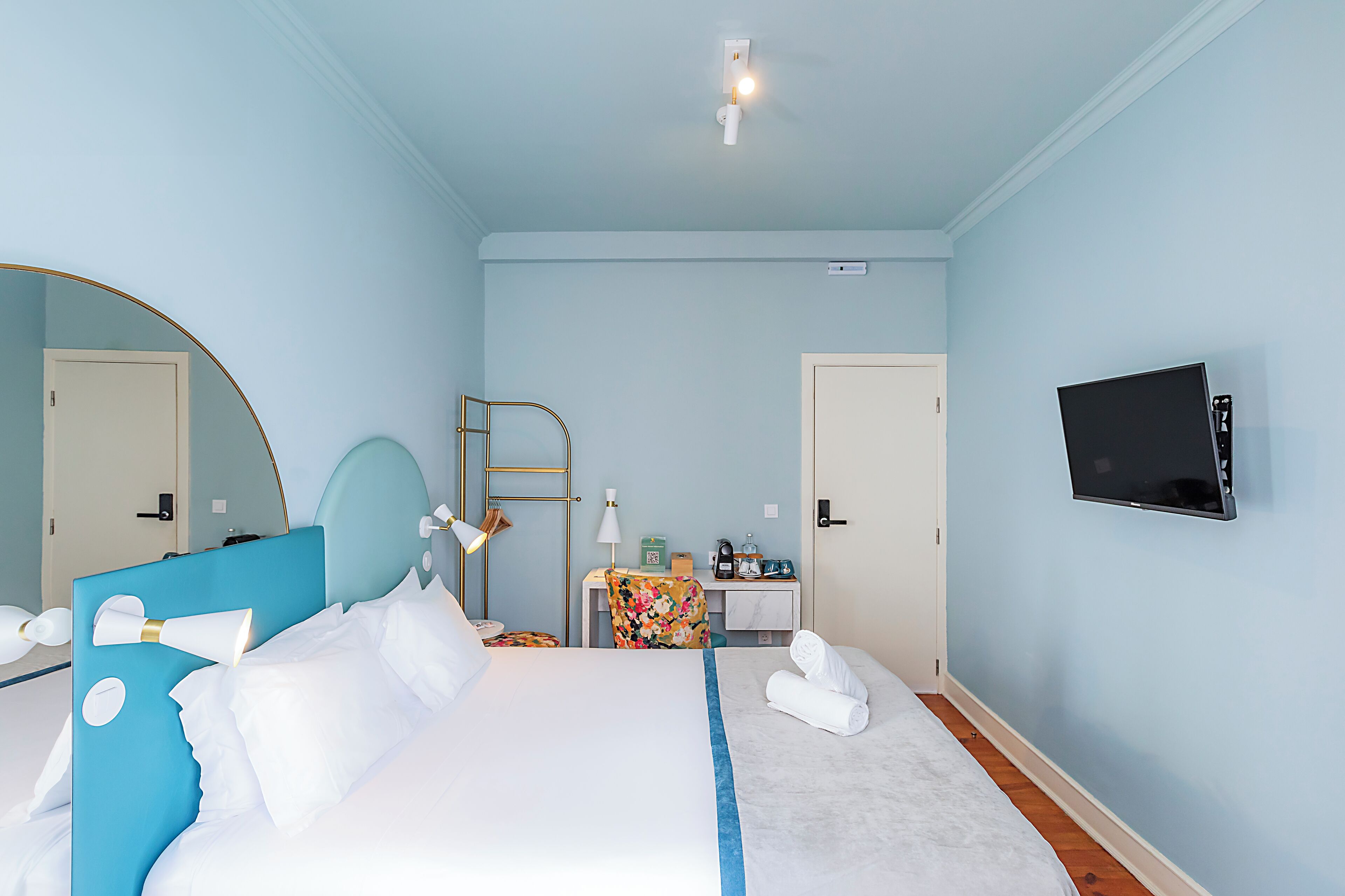 A hotel room with a bed, a desk, a chair, a TV, and a mirror.
