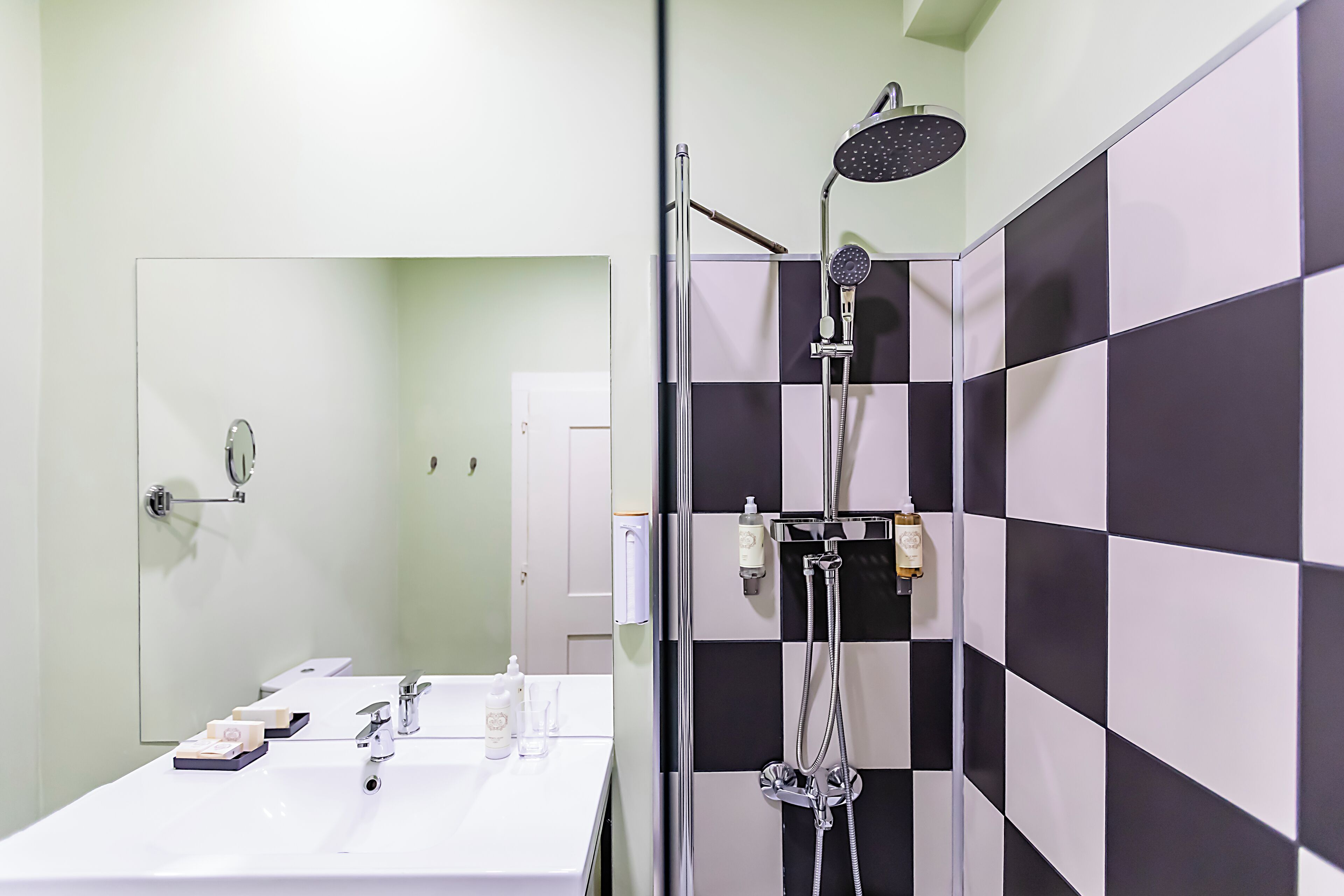 A modern bathroom with a white sink, mirror, and black-and-white checkered shower wall.