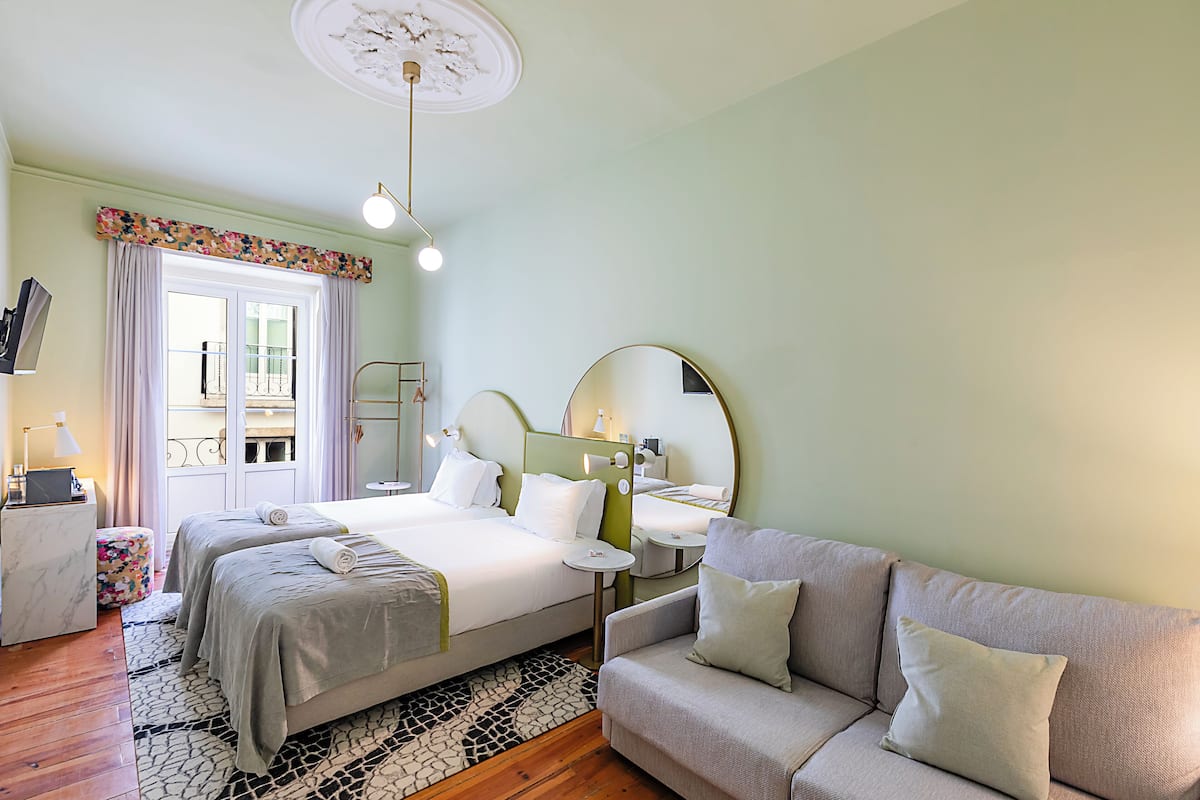 A modern hotel room with a bed, a sofa, a small table, and a mirror.