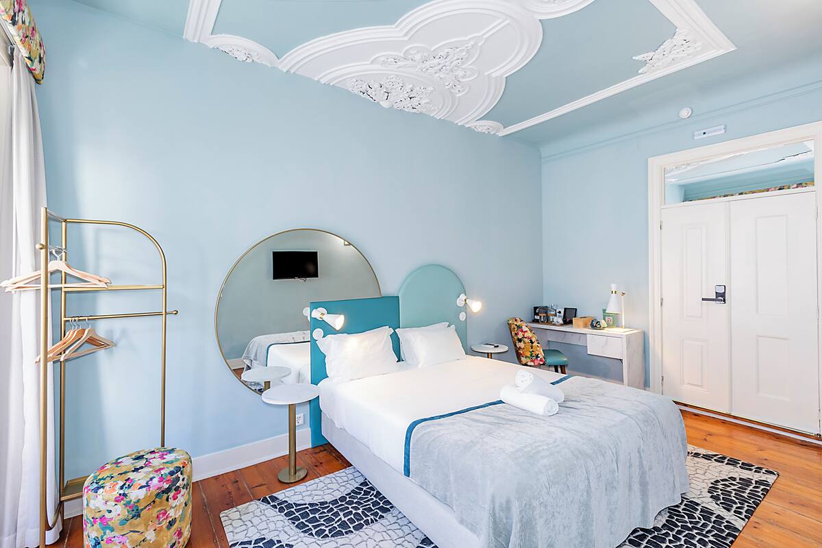 A bedroom with a bed, a round mirror, a bedside table, a wardrobe, and a bathroom with a sink and mirror.