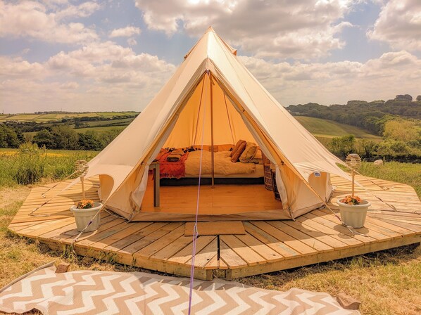 Una tienda en forma de cúpula con una cama en su interior, rodeada por una terraza de madera y una zona cubierta de césped.