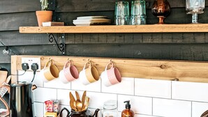 Una cocina con estantes de madera que sostienen diversos objetos, un colgador para ollas y un salpicadero azulejado.