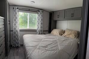 A bedroom with a bed, curtains, a window, and built-in cabinets.