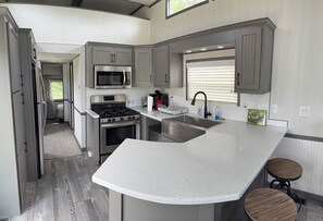 A modern kitchen with a central island, stainless steel appliances, and a window with blinds.