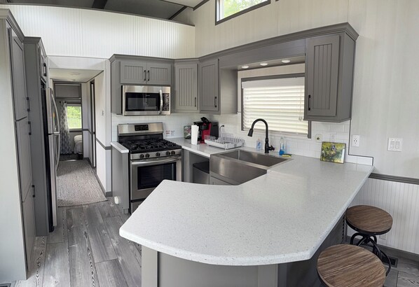 A modern kitchen with a central island, stainless steel appliances, and a window with blinds.