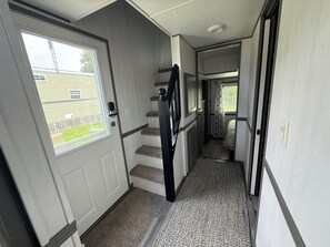 A narrow hallway with a door leading to a bedroom, a small staircase, and a window with blinds. - Cozy Cottage Park Model at Upscale RV Resort in South Haven, Michigan. (South Haven)