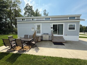 A mobile home with a patio area, a dining table, chairs, and a grill.