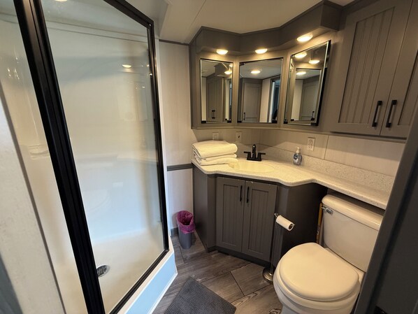 A compact bathroom with a shower, a sink with a mirror, and a toilet. - Cozy Cottage Park Model at Upscale RV Resort in South Haven, Michigan. (South Haven)