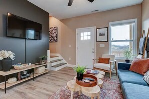 A modern living room with a flat-screen TV, a sofa, a coffee table, and a staircase leading to another level.