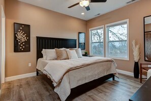 A bedroom with a bed, a ceiling fan, and a window with a view of trees.