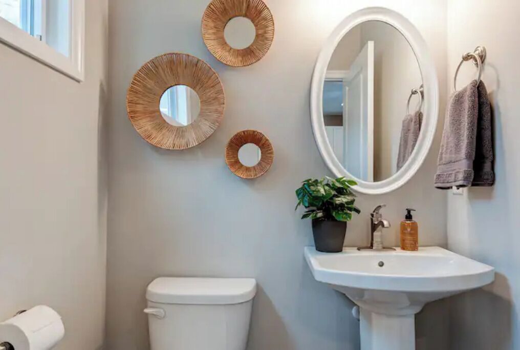 A bathroom with a toilet, sink, mirror, and three wall-mounted circular mirrors.