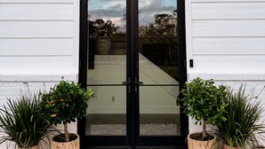 A modern building with a black-framed glass door, white siding, and a gravel pathway with potted plants. - Sebring International Races! (Sebring)