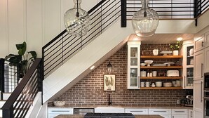 A kitchen with a brick backsplash, white cabinetry, a central island with bar stools, and a staircase with a black railing. - Sebring International Races! (Sebring)