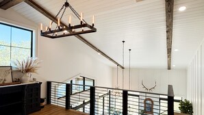 A spacious loft with a high ceiling, exposed beams, and a modern chandelier. A staircase with a metal railing leads to an upper level. - Sebring International Races! (Sebring)