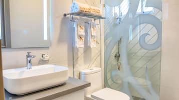 A modern bathroom with a large mirror, a white sink, a toilet, and a glass shower enclosure.