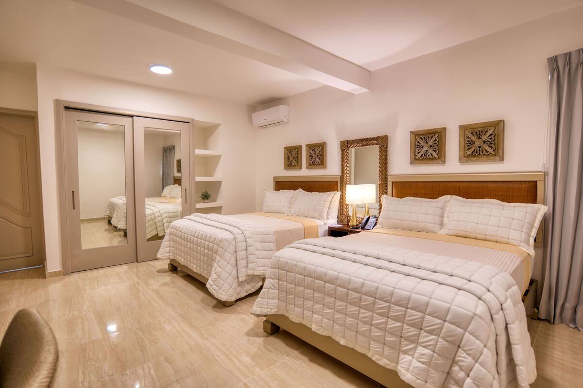 A hotel room with two beds, a mirror, a bedside table, and a wardrobe.
