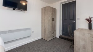 Ein modernes Zimmer mit flachbildfernseher an der Wand, einem Holzschrank, einer Tür, einem Heizkörper und einem kleinen Tisch mit einer Vase.