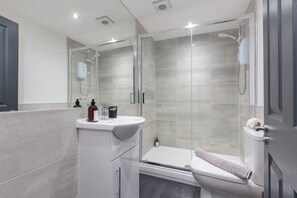 A modern bathroom with a glass-enclosed shower, a white sink, and a toilet.