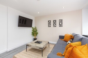 A modern living room with a grey sofa, orange cushions, a wooden coffee table, and a potted plant.