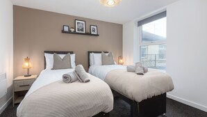 Ein Hotelzimmer mit zwei Betten, Nachttischlampen, einem Fenster mit Blick und Wandbildern.