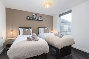 A hotel room with two beds, bedside lamps, a window with a view, and wall-mounted artwork.