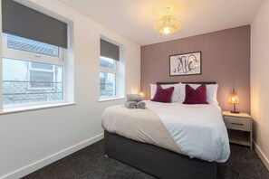 A neatly made bed with a white comforter and two pillows, a bedside lamp, and a framed artwork on the wall.