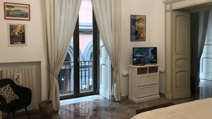 A hotel room with a large window, a television on a white cabinet, a black chair, and a bed. - Lovely apartment Residenze Pessina Naples Historic Center (Napoli)