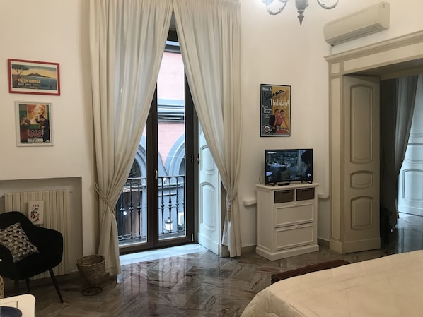 Une chambre d’hôtel avec une grande fenêtre, un téléviseur posé sur un meuble blanc, une chaise noire et un lit.