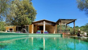 A pool area with clear water, lounge chairs, and a building with a stone facade. - Busqueroles Petit - Two Bedroom Villa, Sleeps 4 (Pollença)