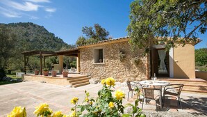 A stone house with a patio, outdoor seating, and a mountain backdrop. - Busqueroles Petit - Two Bedroom Villa, Sleeps 4 (Pollença)