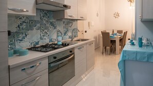 Una cocina moderna con estufa a gas, horno y pileta, un comedor con mesa y sillas, y azulejos decorativos en la pared.
